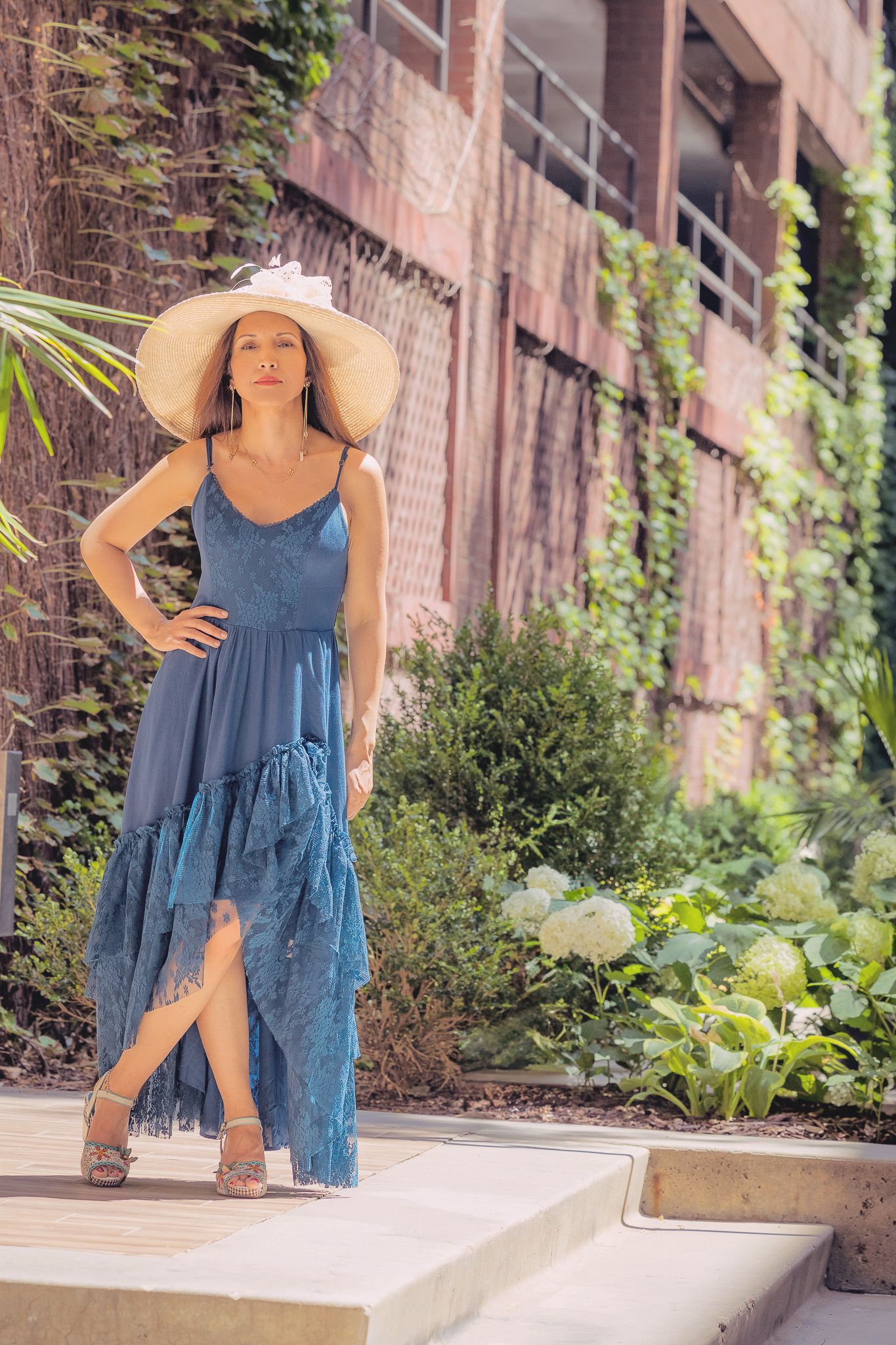 A carefree summer scene of someone in a flowy blue dress dancing and twirling outdoors near a brick building.
