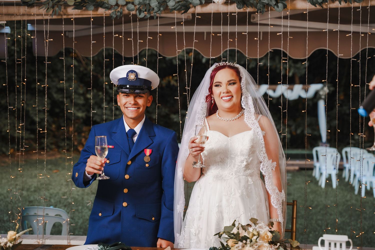 A joyful wedding couple toasting with champagne glasses in an outdoor garden setting.
