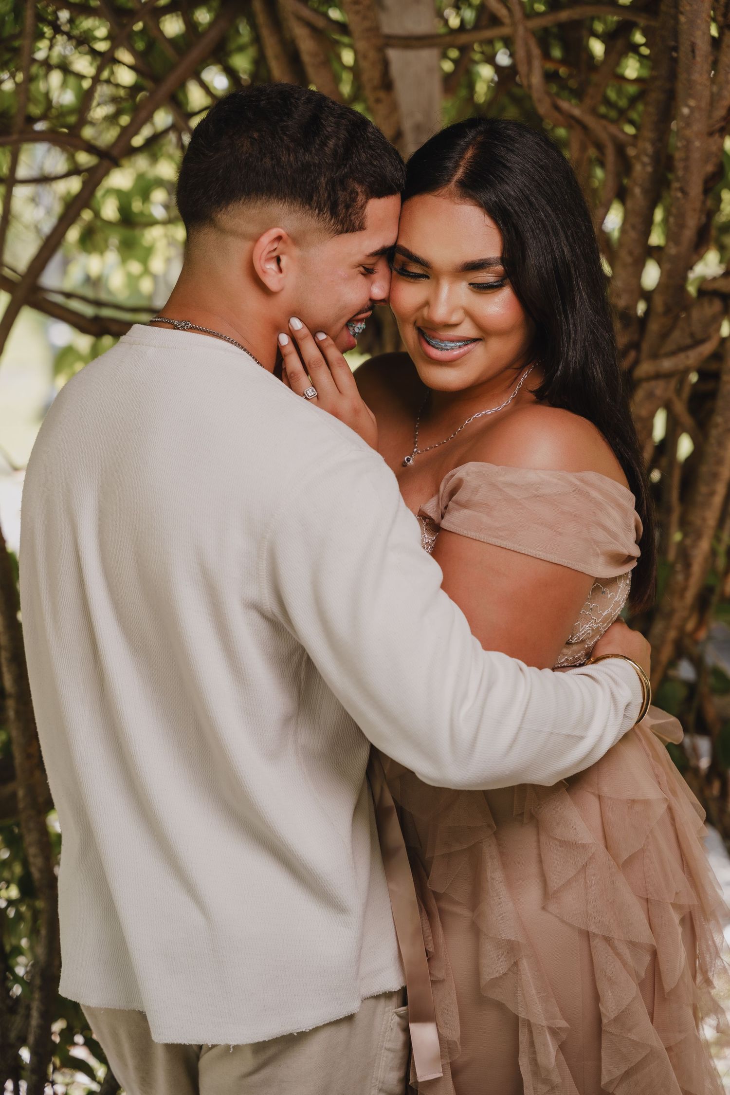 A romantic couple sharing an intimate moment among garden foliage wearing coordinated neutral-toned outfits.