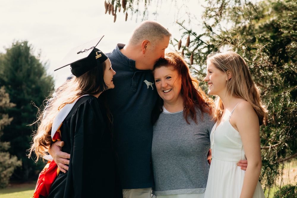 A family of four, where the dad is kissing the mom and their grown girls look on smiling