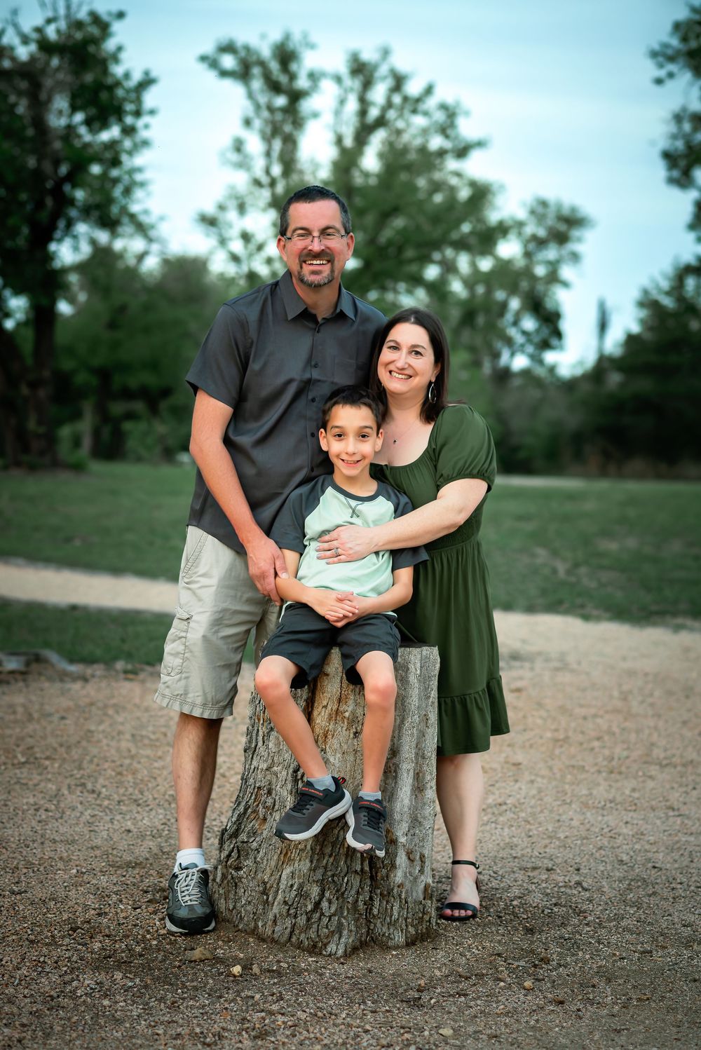 A family of three with a young son resting on a log where the parents are posed and each side of him