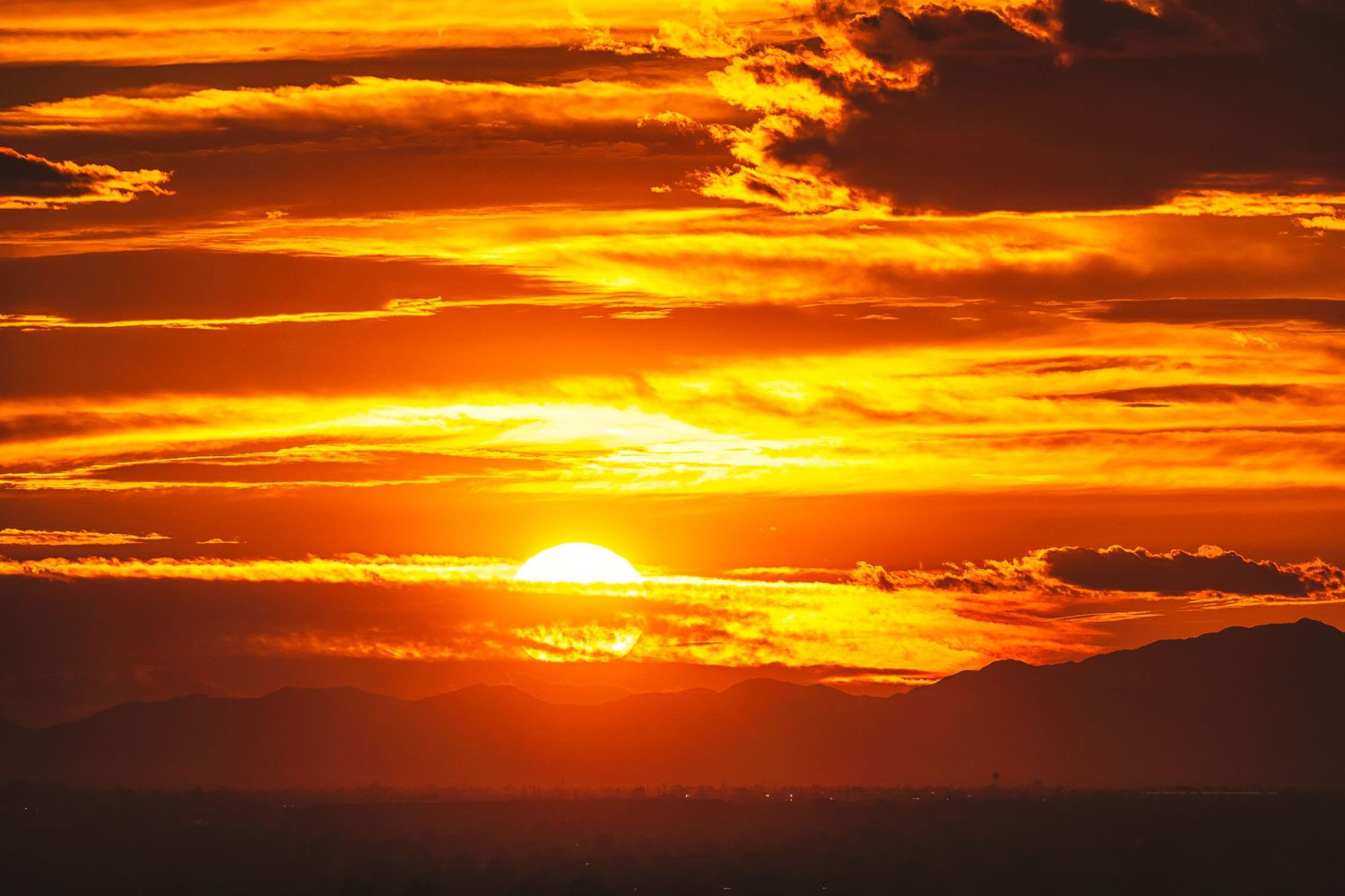 Dramatic orange and red sunset sky with dark clouds and bright sun on the horizon.