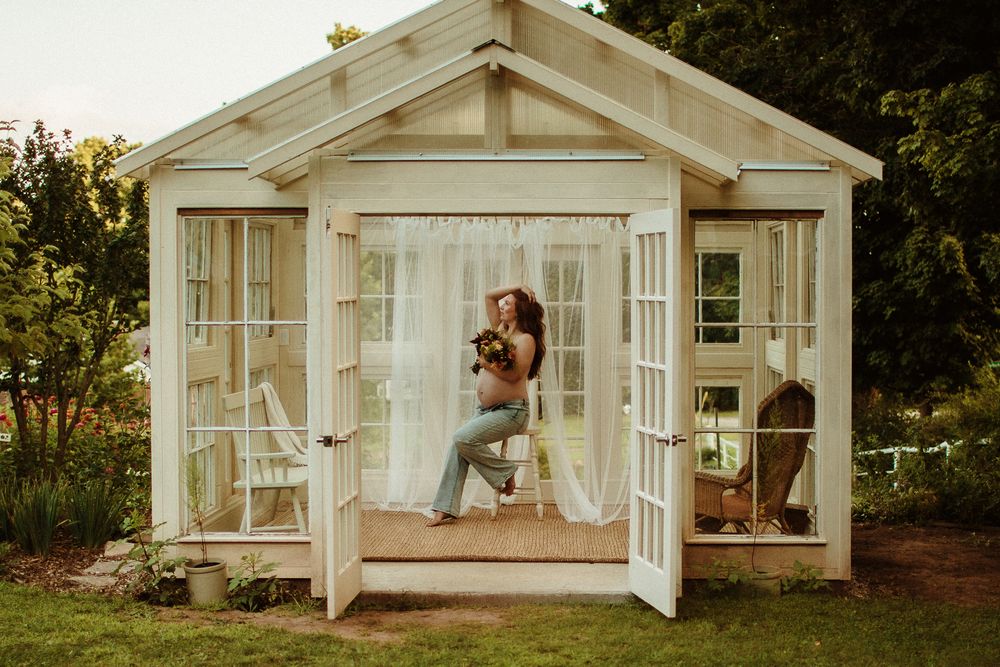 A rustic white wooden greenhouse structure in a garden setting.