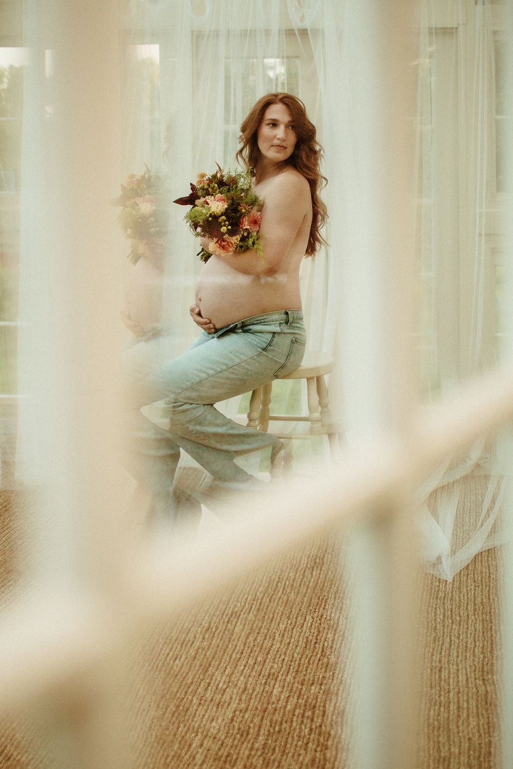 Maternity portrait with woman holding flower bouquet in sunlit room.