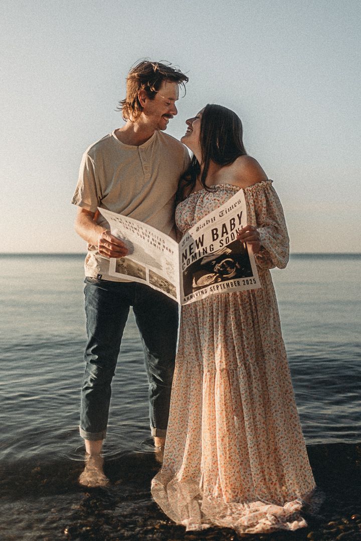 Couple shares intimate moment while reading newspaper together on beach at sunset.