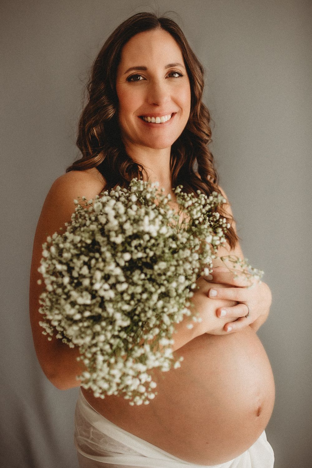 Pregnant woman holding baby's breath flowers in flowing white dress.
