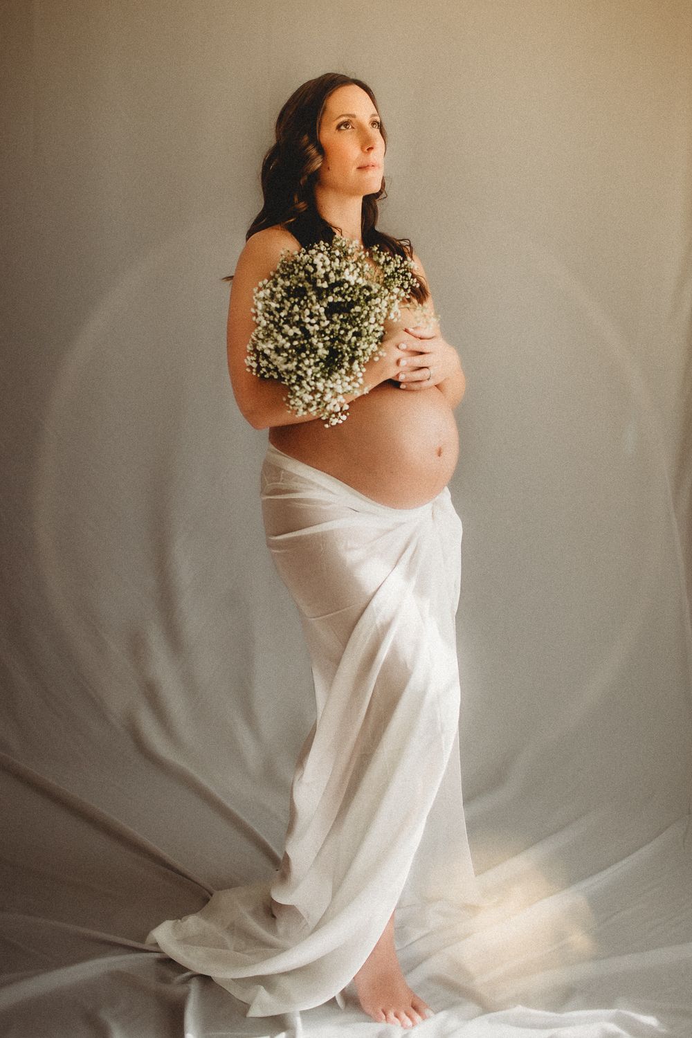 Ethereal maternity portrait with flowing white fabric and natural lighting.