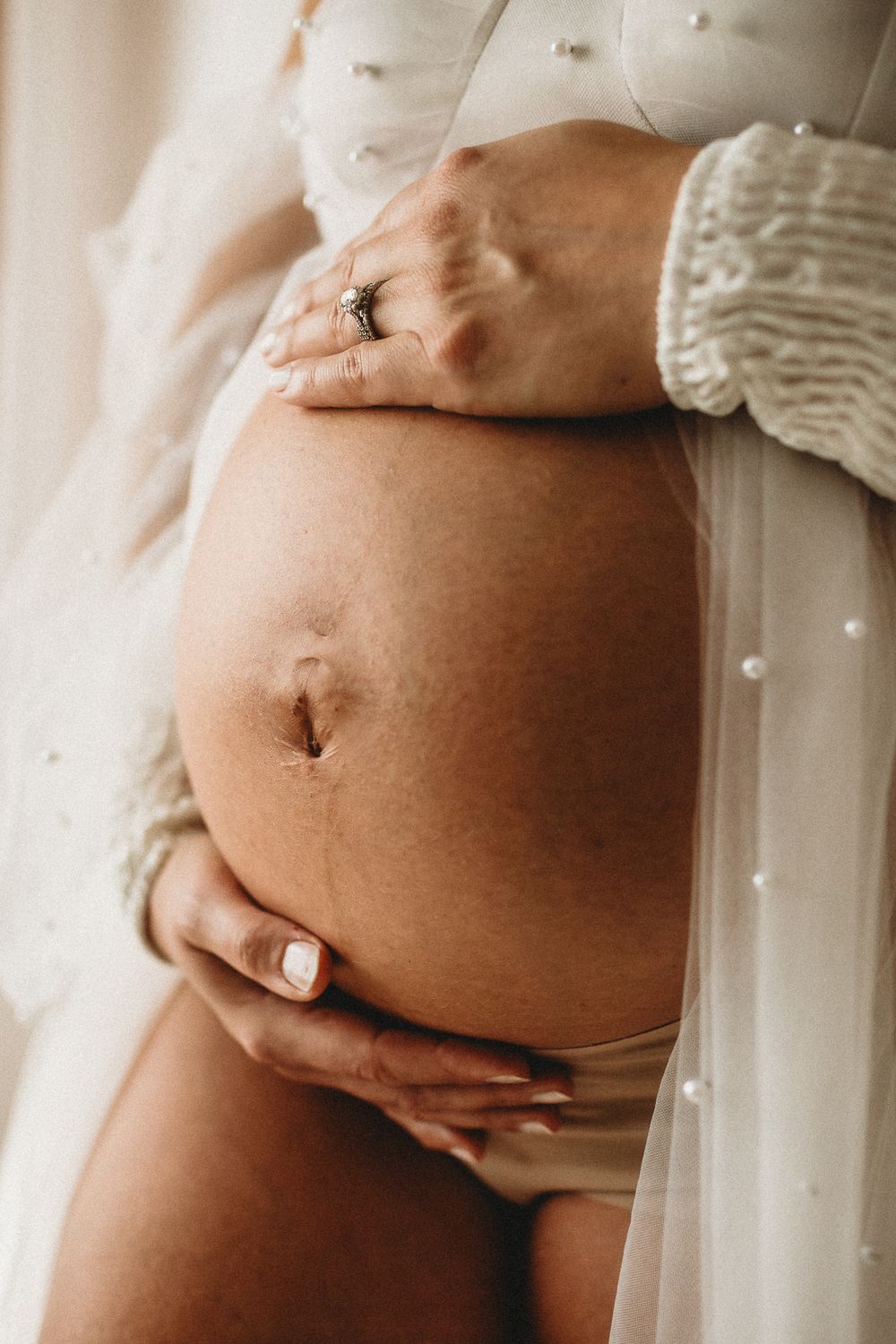 Close-up details of pregnant belly with white knit sweater.