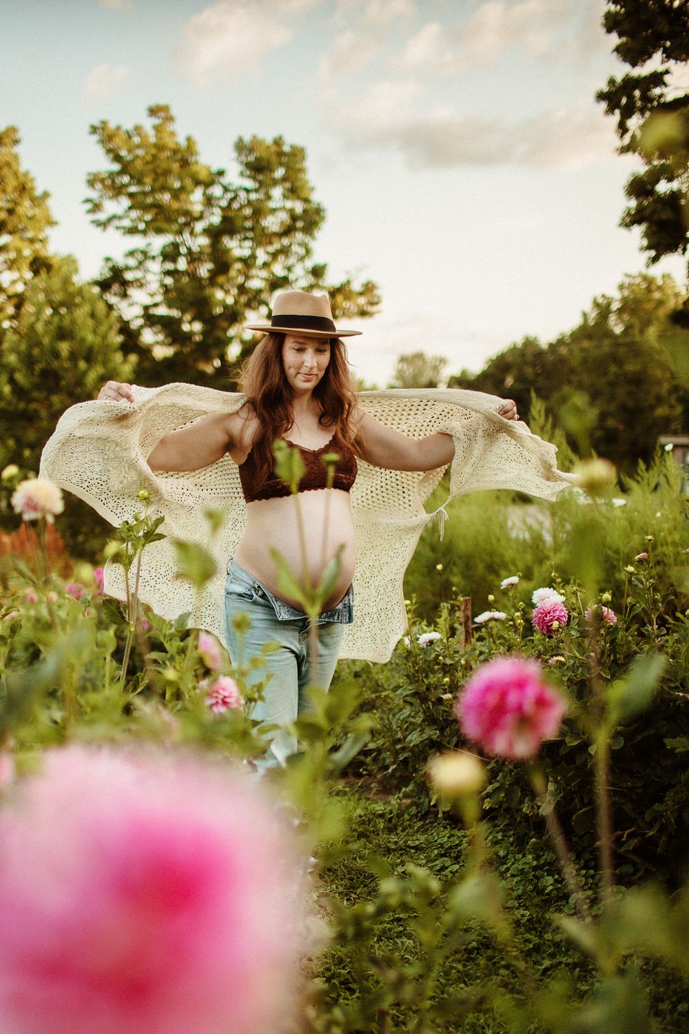 Pink flowers bloom in foreground of garden with flowing white lace and denim outfit.