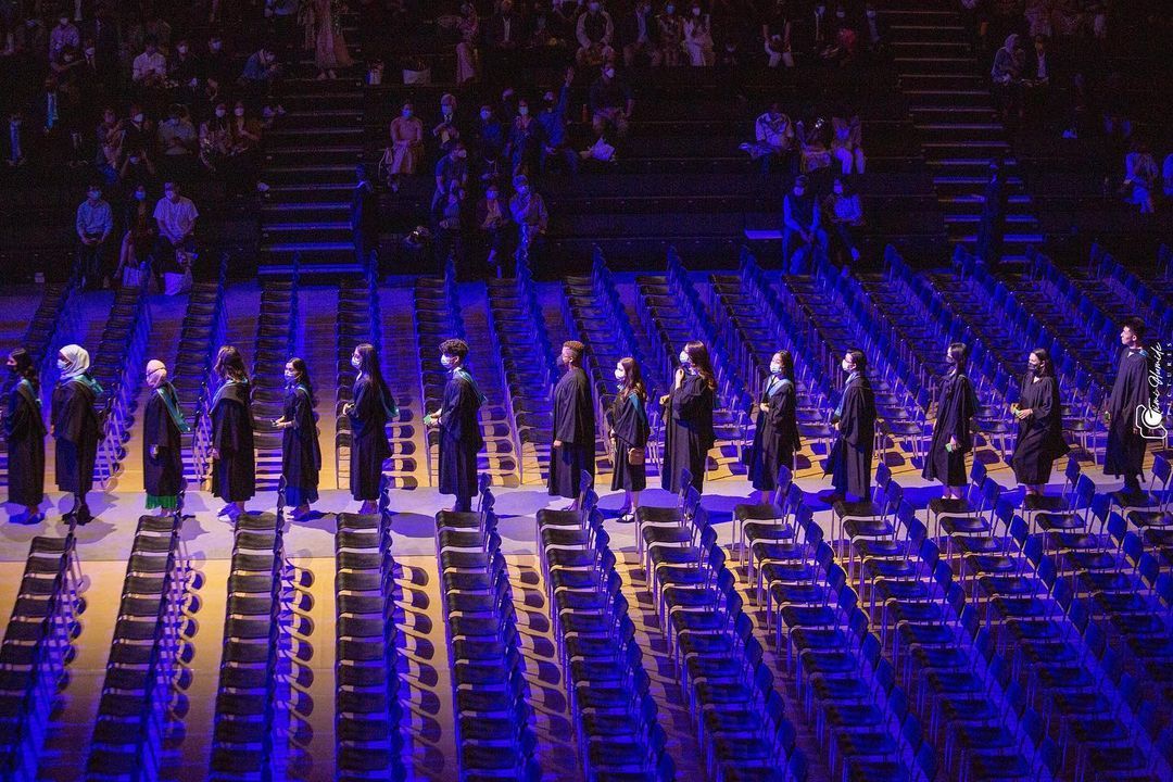 Performers stand in formation on a dark stage illuminated by dramatic blue lighting.