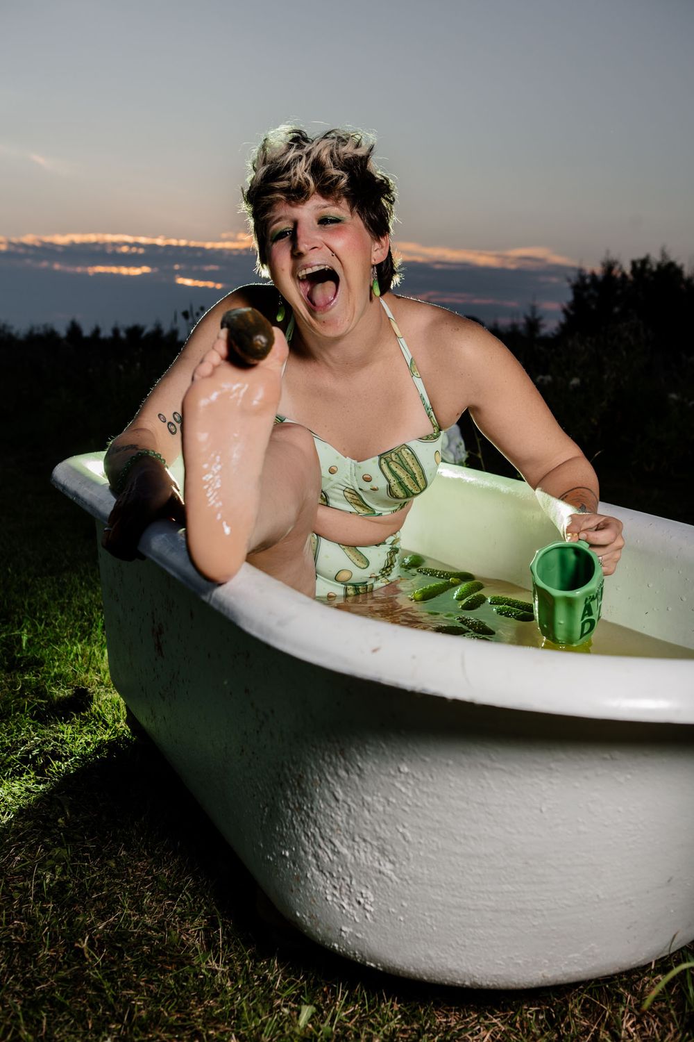 Playful outdoor bathtub photo shoot with vintage tub and pickle-themed props at sunset.