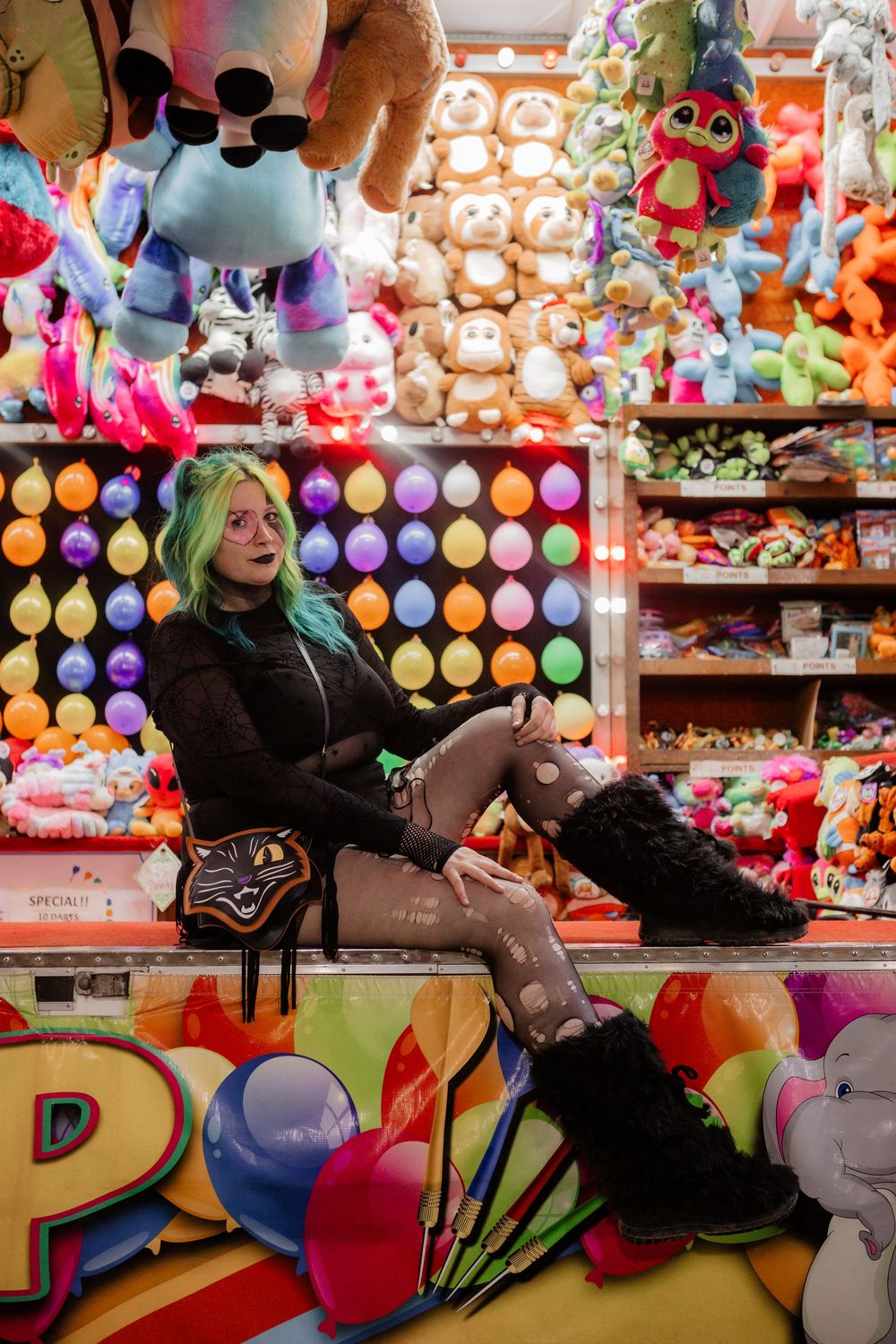 Carnival scene with colorful plush toys and person posing against wall of stuffed animals.
