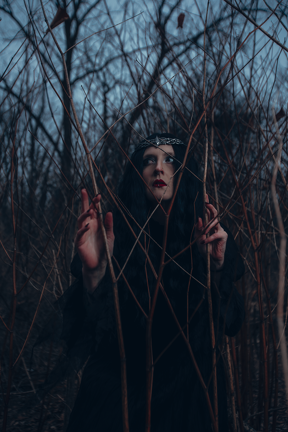 Moody portrait through bare winter branches with dark clothing and atmospheric lighting.