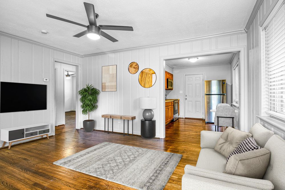 Bright living room interior with hardwood floors, ceiling fan, and large windows letting in natural light.