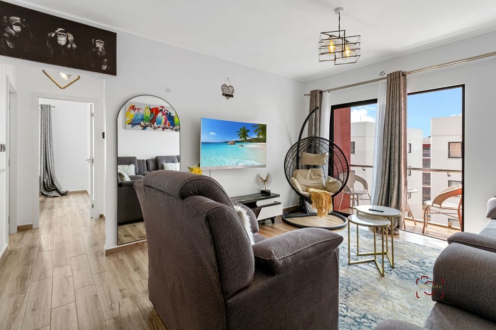 A modern apartment interior showcasing light wood flooring, gray furniture, and contemporary decor with large windows.