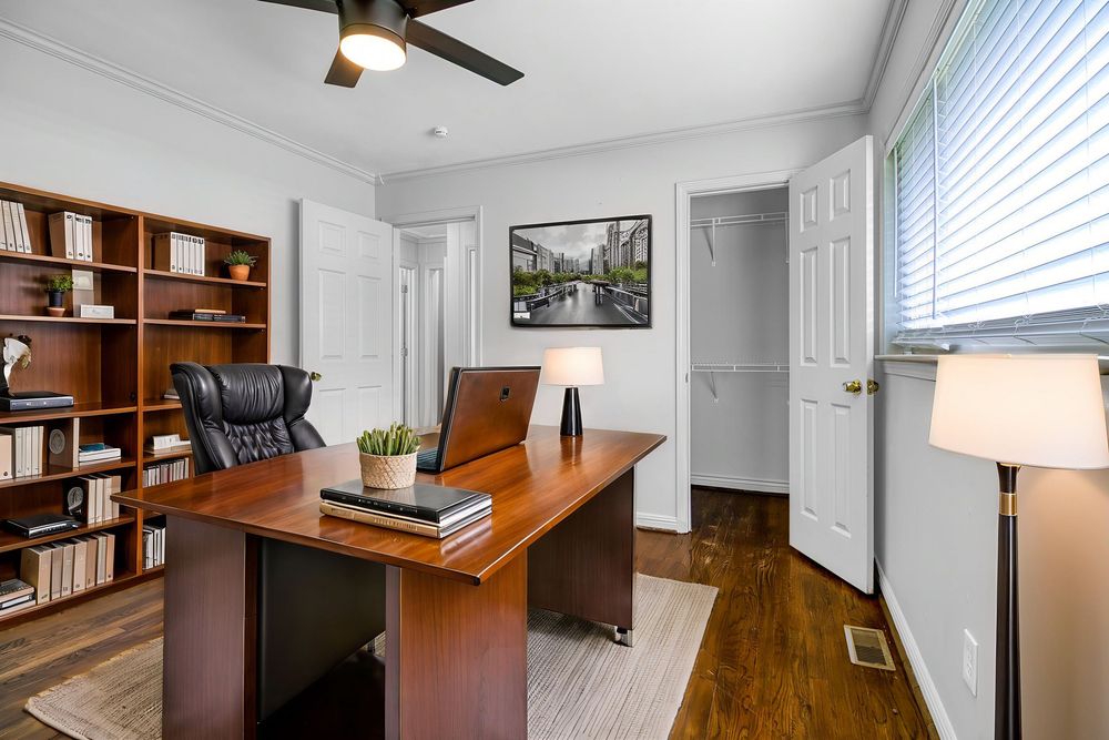 Modern home office with hardwood floors, white walls, built-in shelving, and a wooden desk illuminated by natural light.