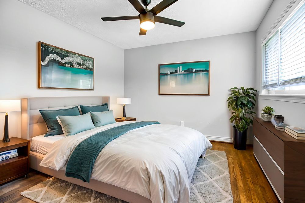 Modern bedroom with teal accents features hardwood floors, ceiling fan, and natural light from white-trimmed windows.