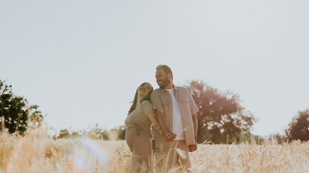 Silhouetted couple poses in golden field during sunset with trees in background.
