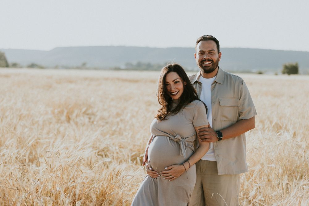 Maternity photoshoot in a sun-drenched wheat field with mountains on the horizon.