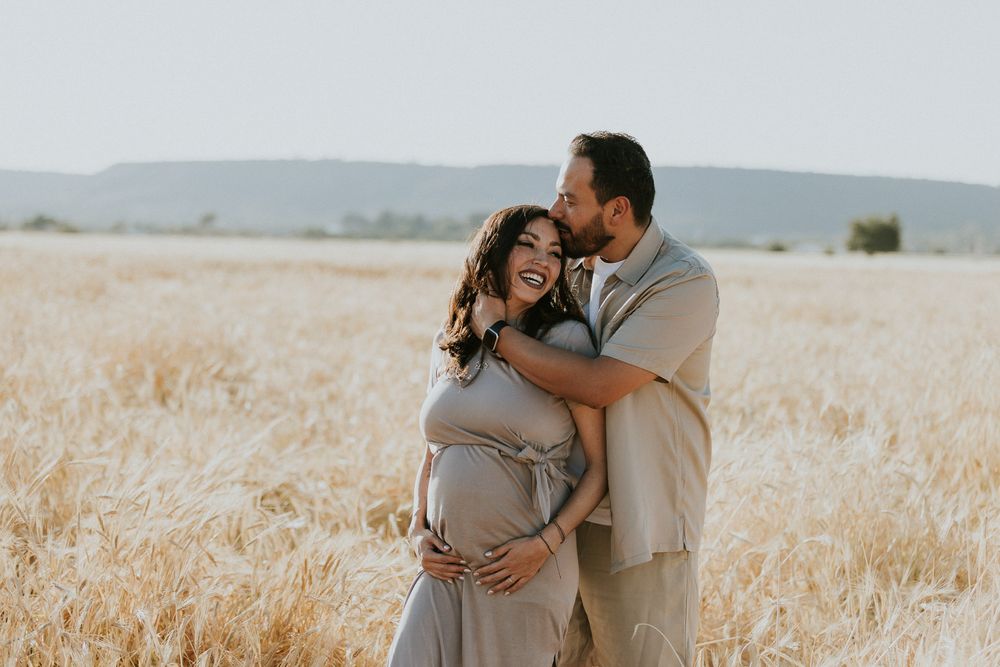 Tender embrace during maternity photoshoot in golden wheat field.