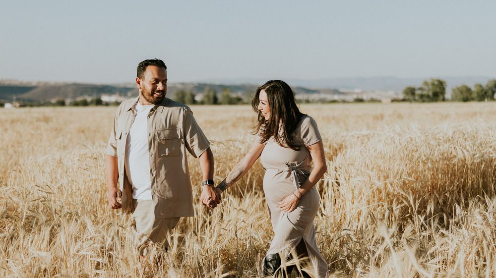 Couple strolls hand in hand through a golden wheat field at sunset.