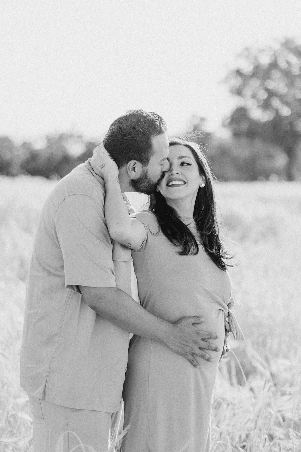 Intimate black and white portrait of an expecting couple embracing in a sunny field.