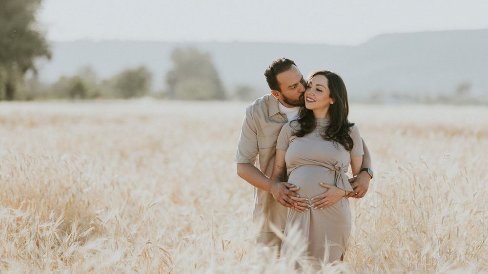 Intimate maternity photo session in a rustic wheat field with distant mountains.