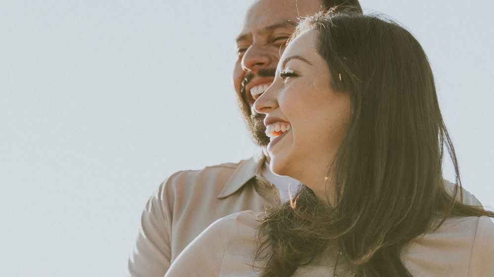 Couple shares joyful laughter together in bright natural sunlight.