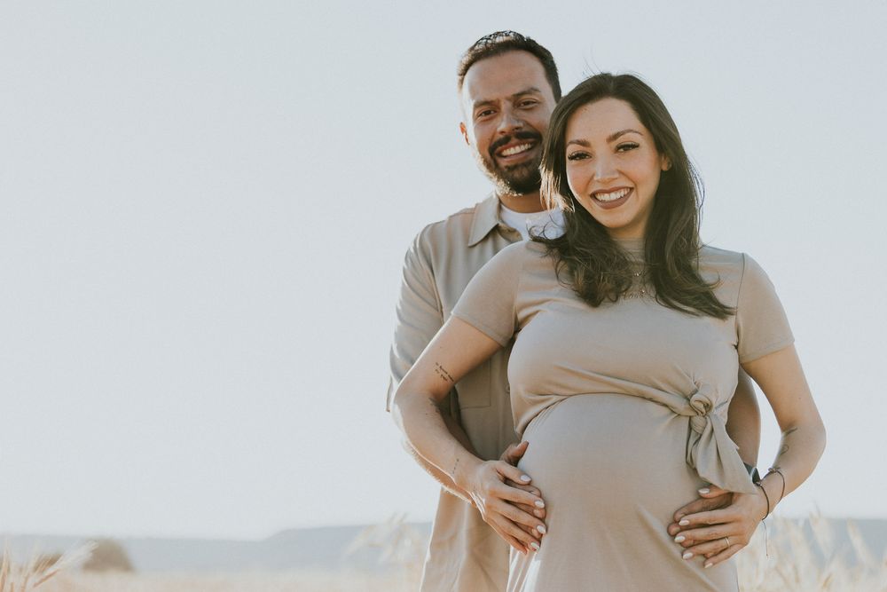 A maternity portrait of a couple posing together in warm sunlight.