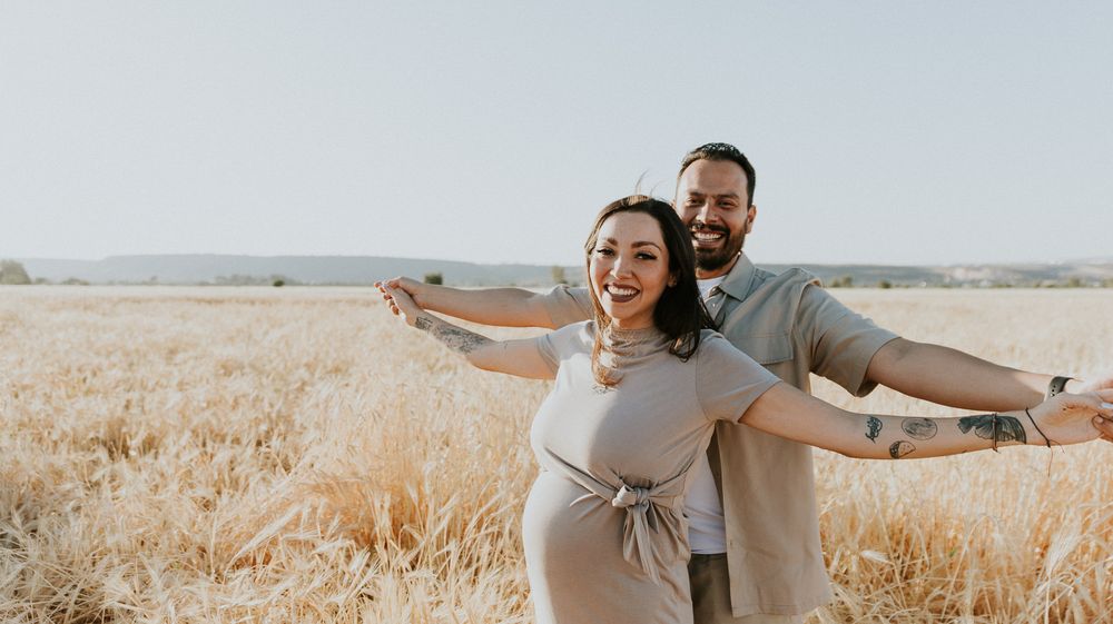 Happy couple spreads their arms wide in a sun-lit field of wheat.