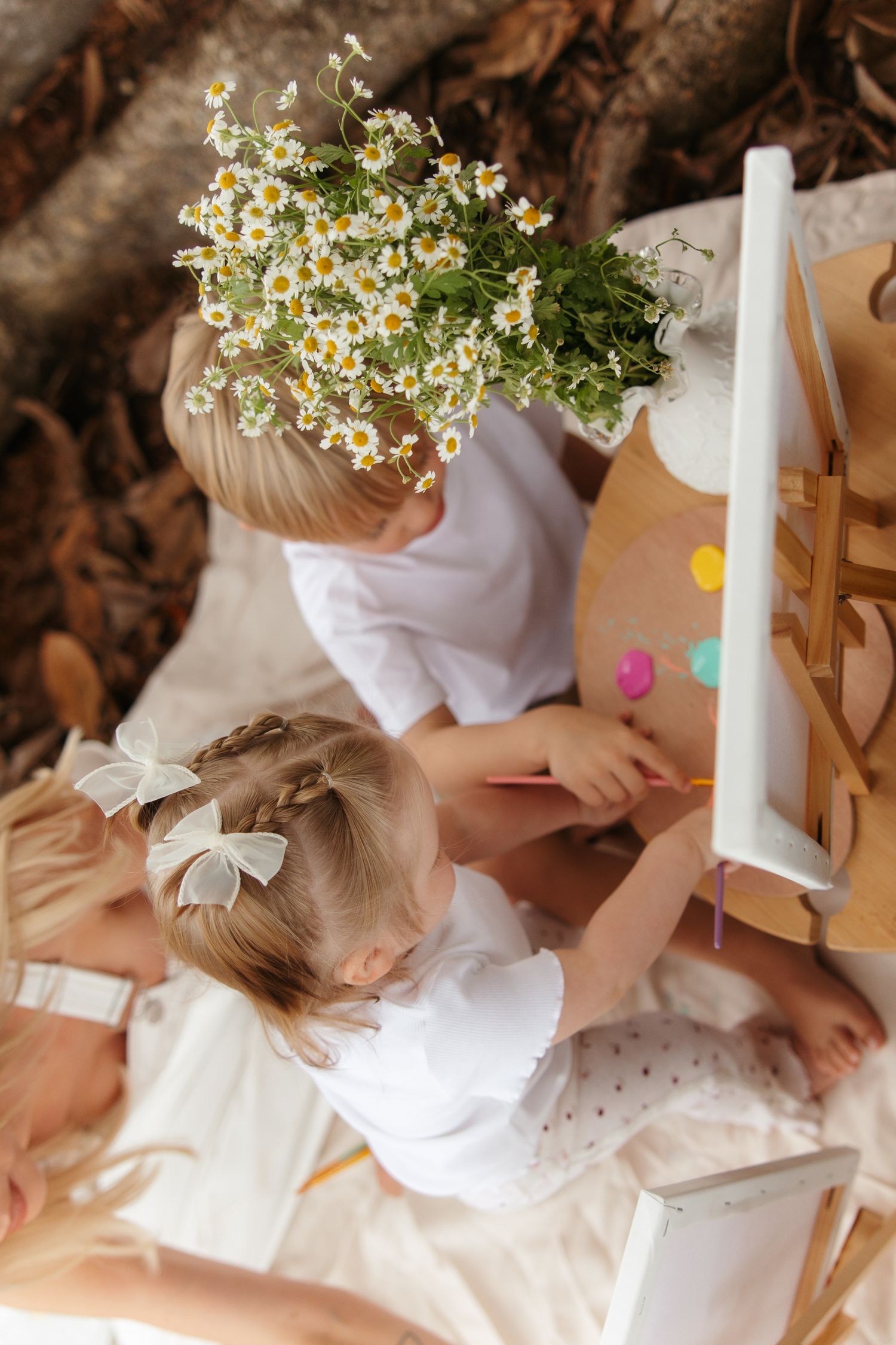 A vintage book and vase of flowers sit beneath a massive tree with sprawling roots and branches in dappled sunlight.