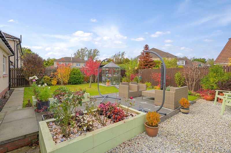 A panoramic view of a landscaped garden with stone pathways, potted plants, and colorful shrubs under a blue sky.