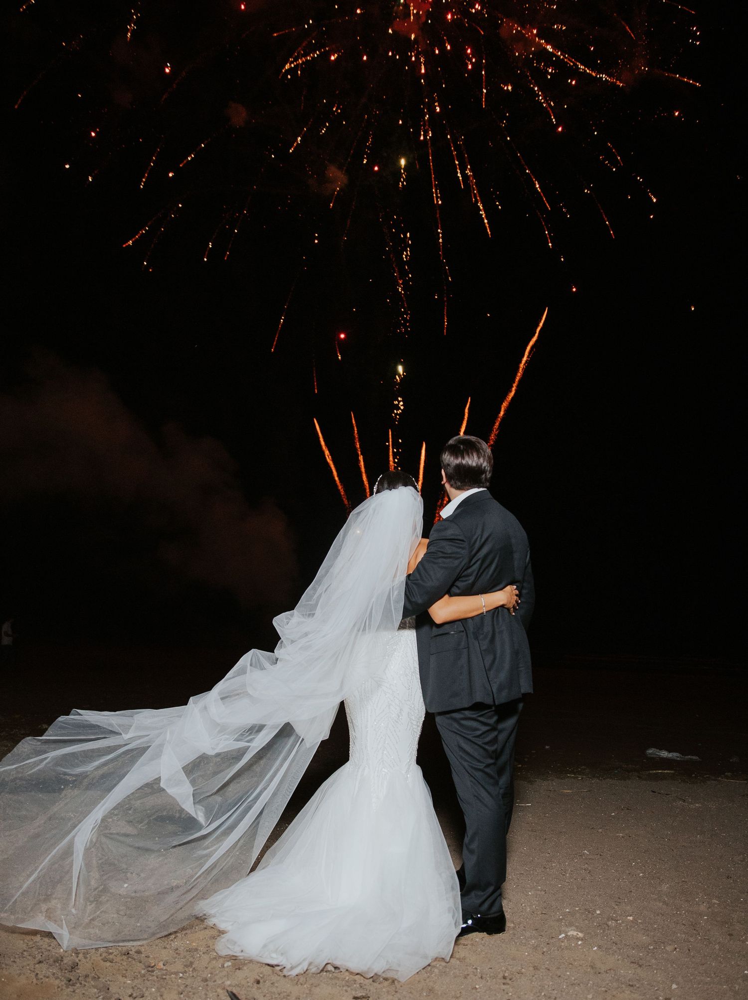 A couple embracing under red fireworks display against a dark night sky.
