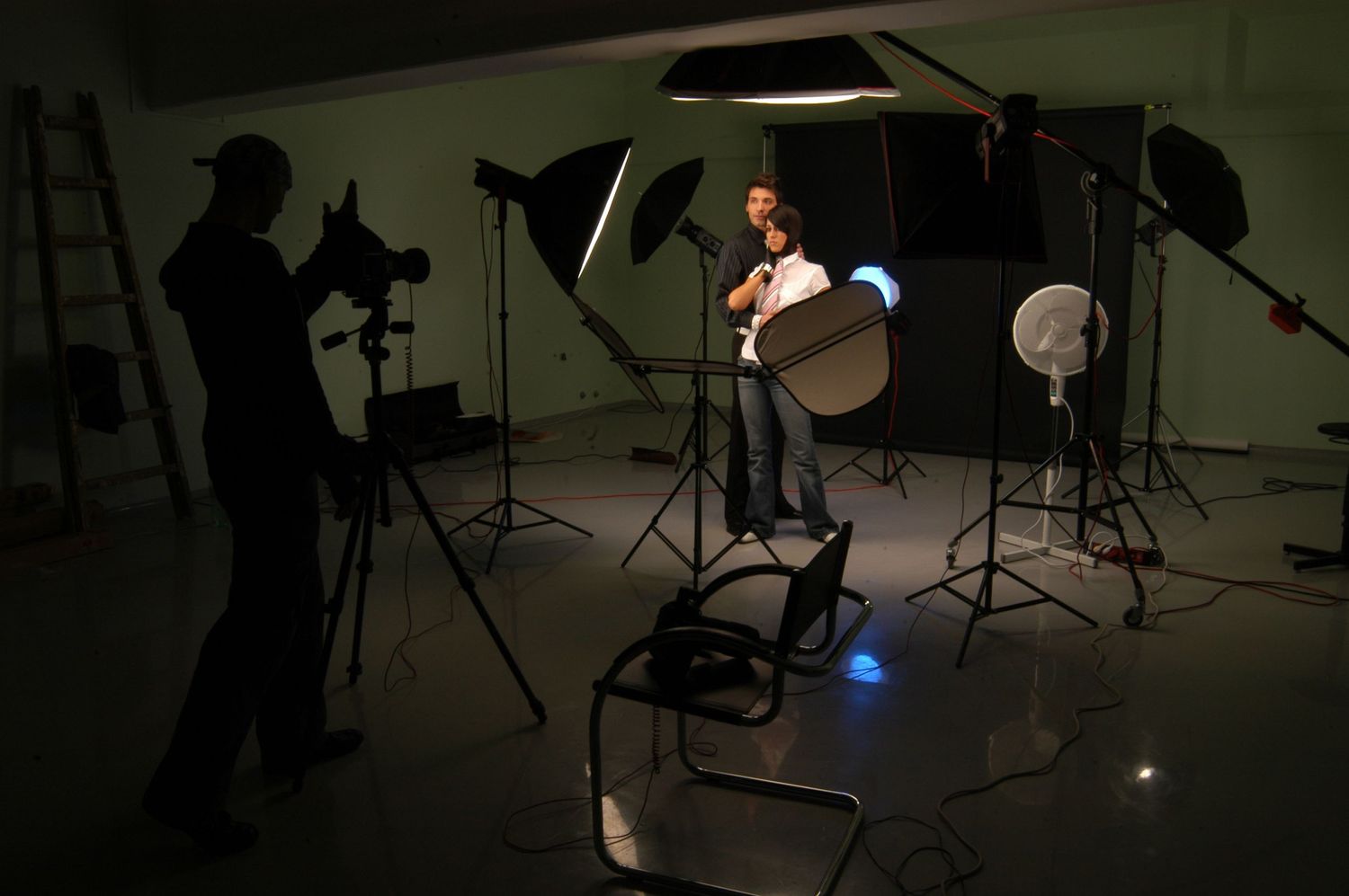 Behind the scenes photo shoot setup with lighting equipment and silhouetted crew in dark studio.