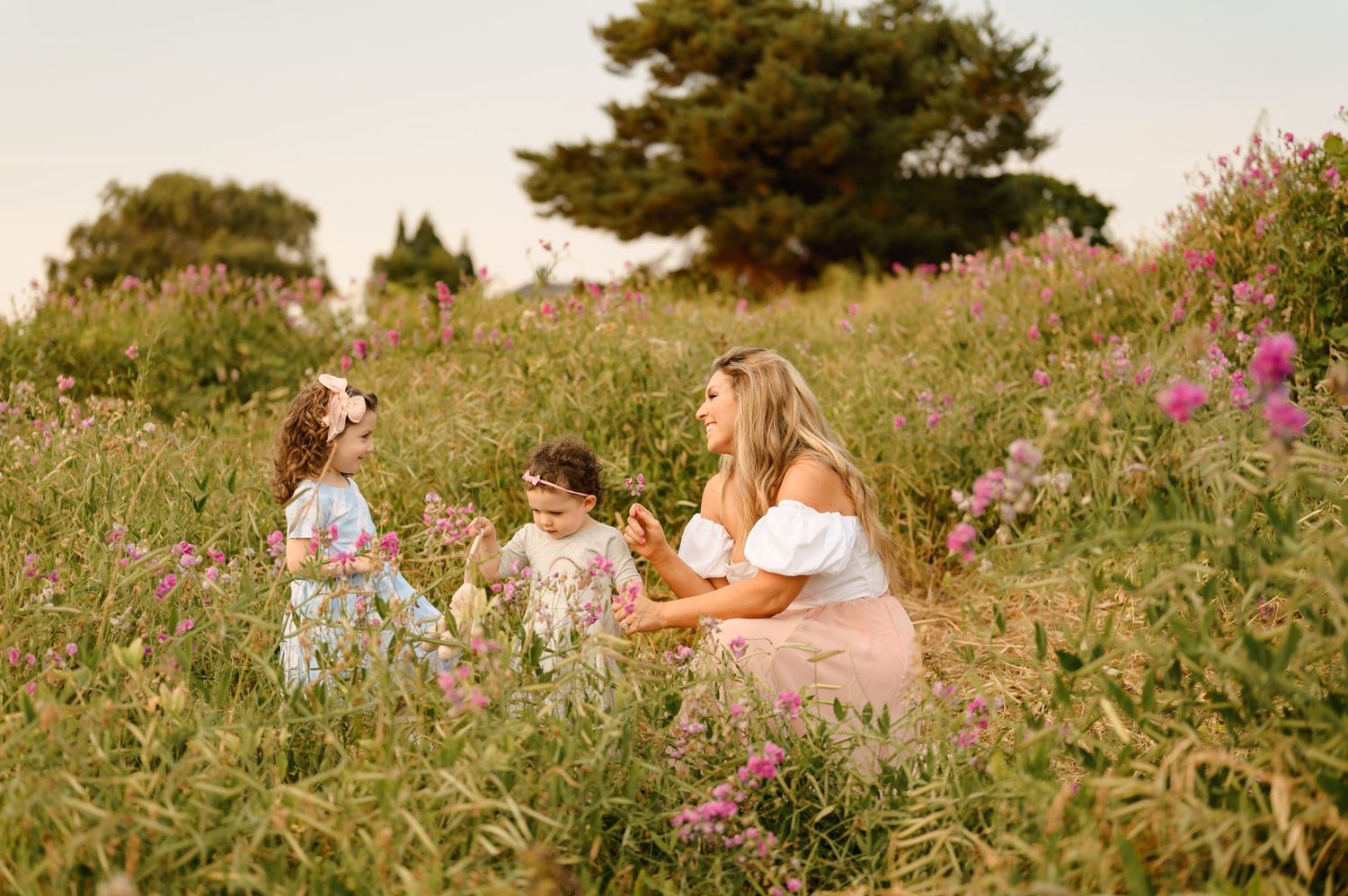 A woman and two children enjoying time together in a flower-filled meadow at dusk.