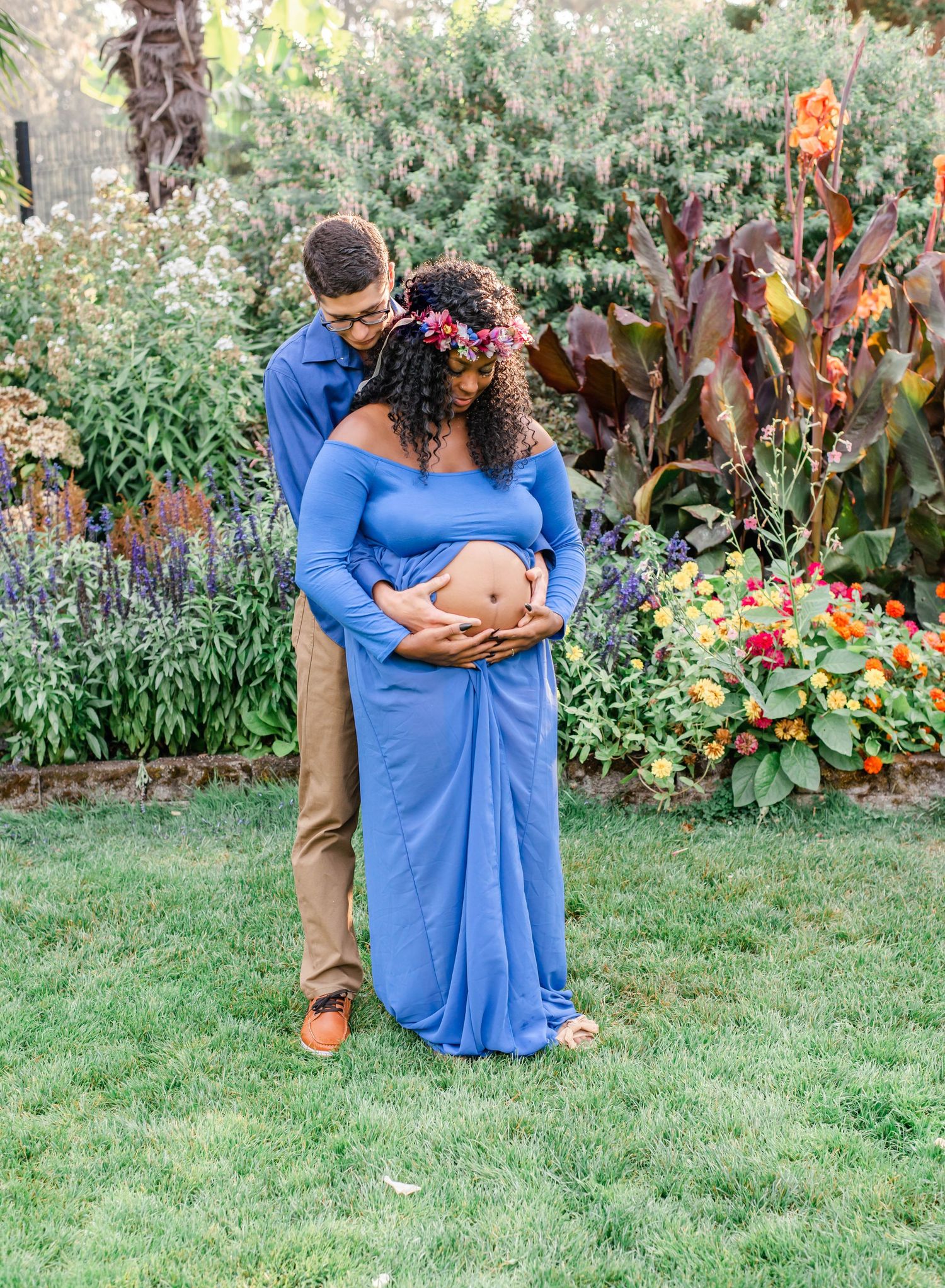 Maternity photo of couple embracing in lush garden with colorful flowers.