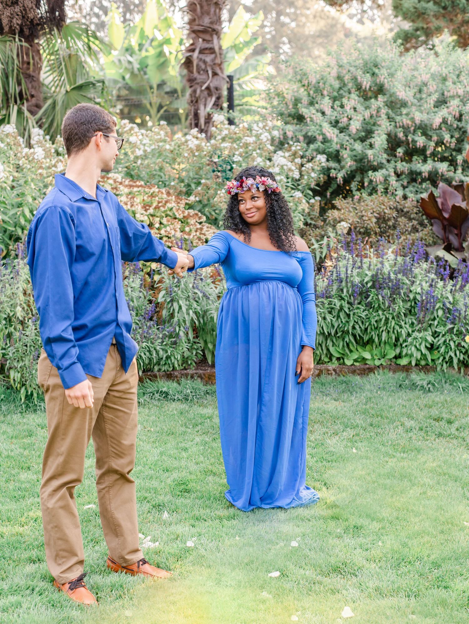 A couple in matching blue outfits share a romantic moment during their maternity shoot in a garden.