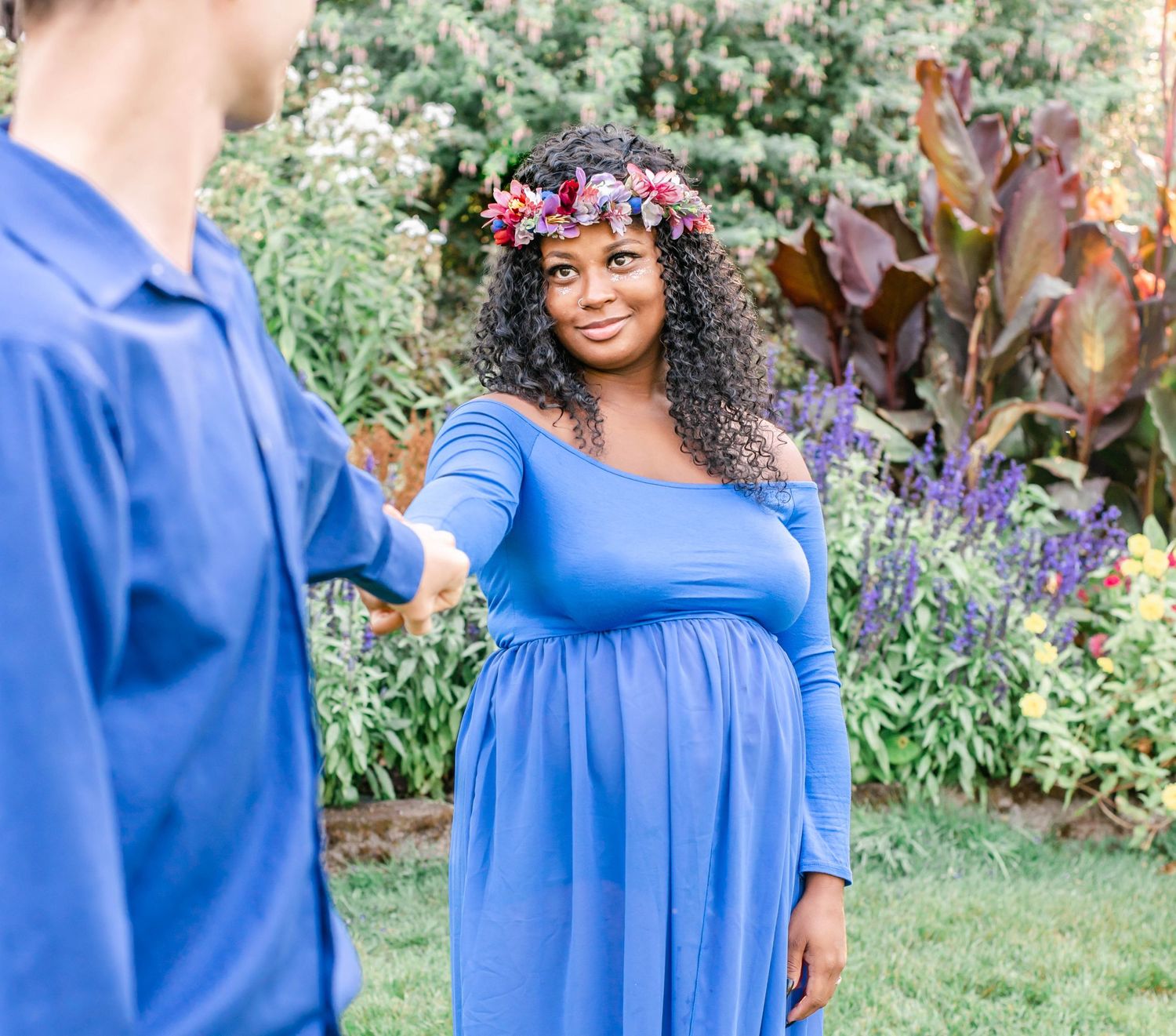 A close-up maternity photo shows a couple dancing in a garden with vibrant flowers.