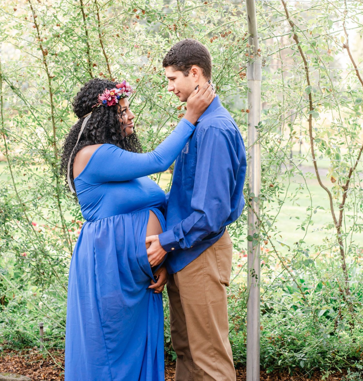A romantic maternity moment captured in a wooded setting with a couple in coordinating blue outfits.