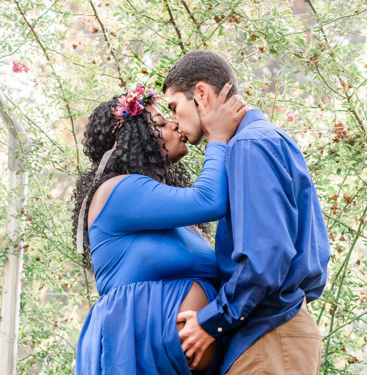 An intimate moment between an expectant couple in a garden setting with blooming trees.