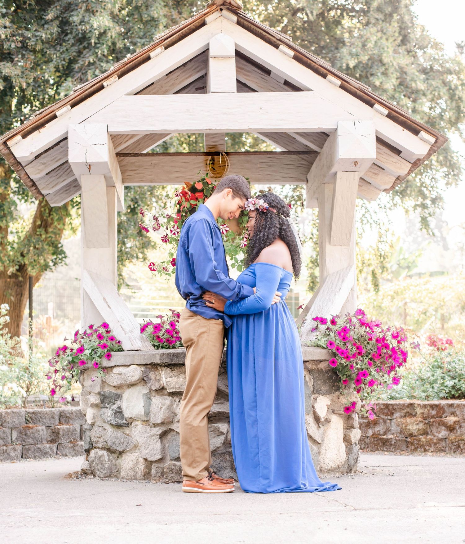 A romantic maternity photo under a white gazebo decorated with pink flowers.