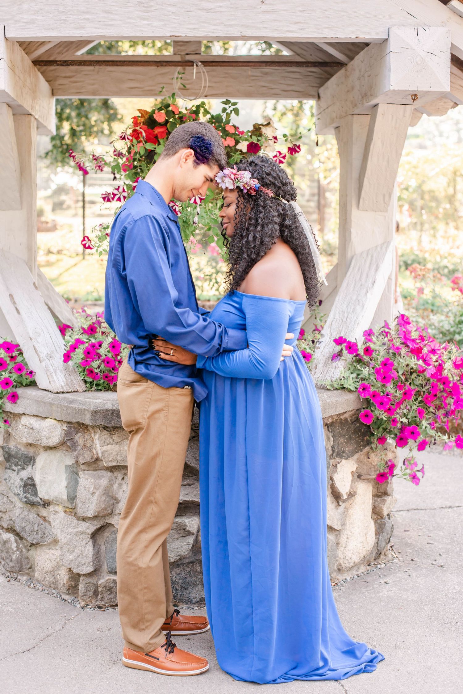 An intimate maternity moment captured under a stone gazebo with flowering plants.