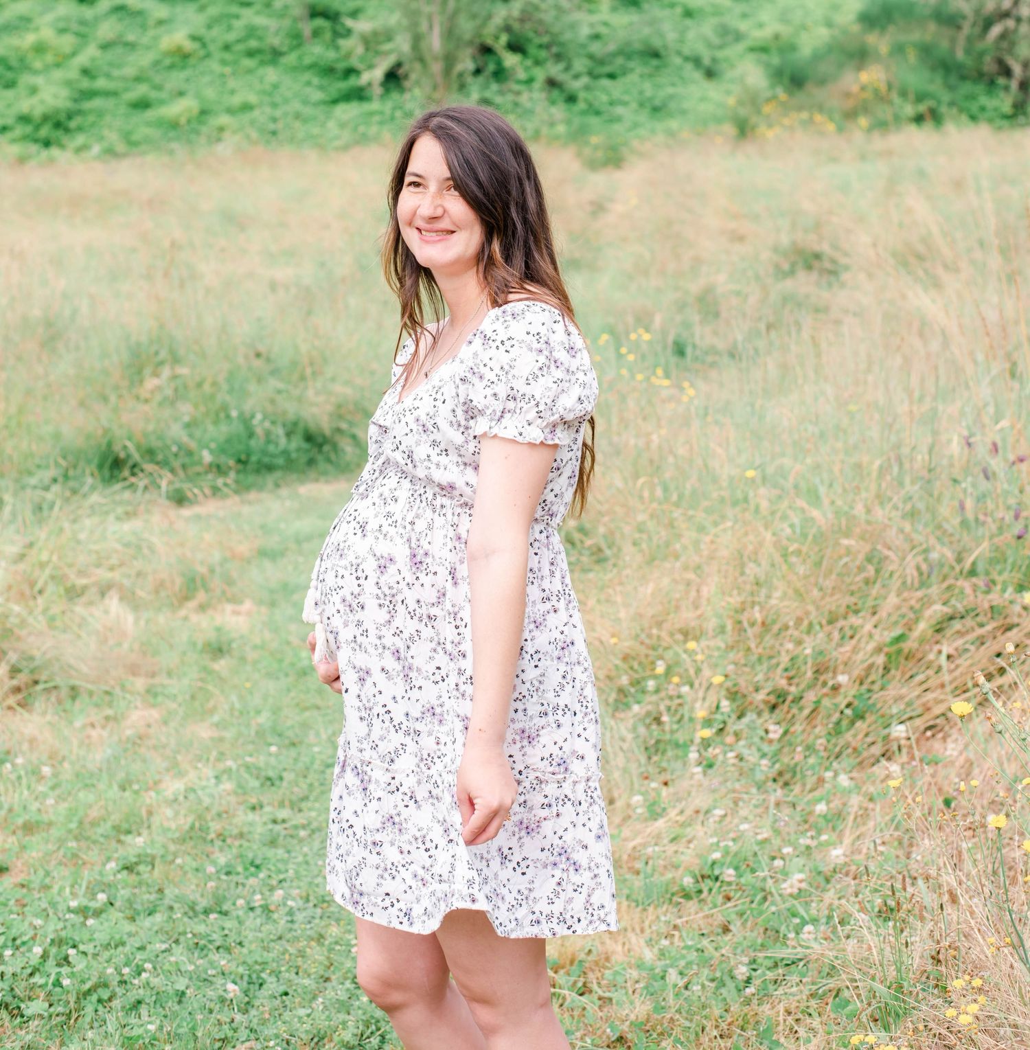 Candid outdoor portrait session showing someone in a white floral dress against green foliage.