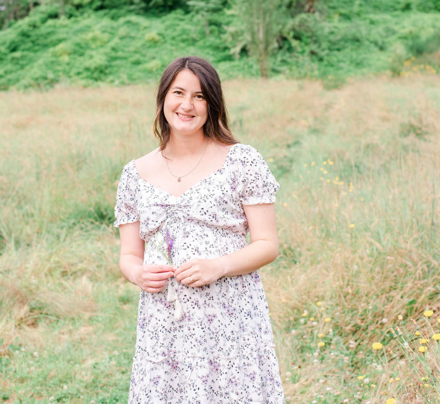 Summer photoshoot in a field with someone wearing a delicate white patterned dress.