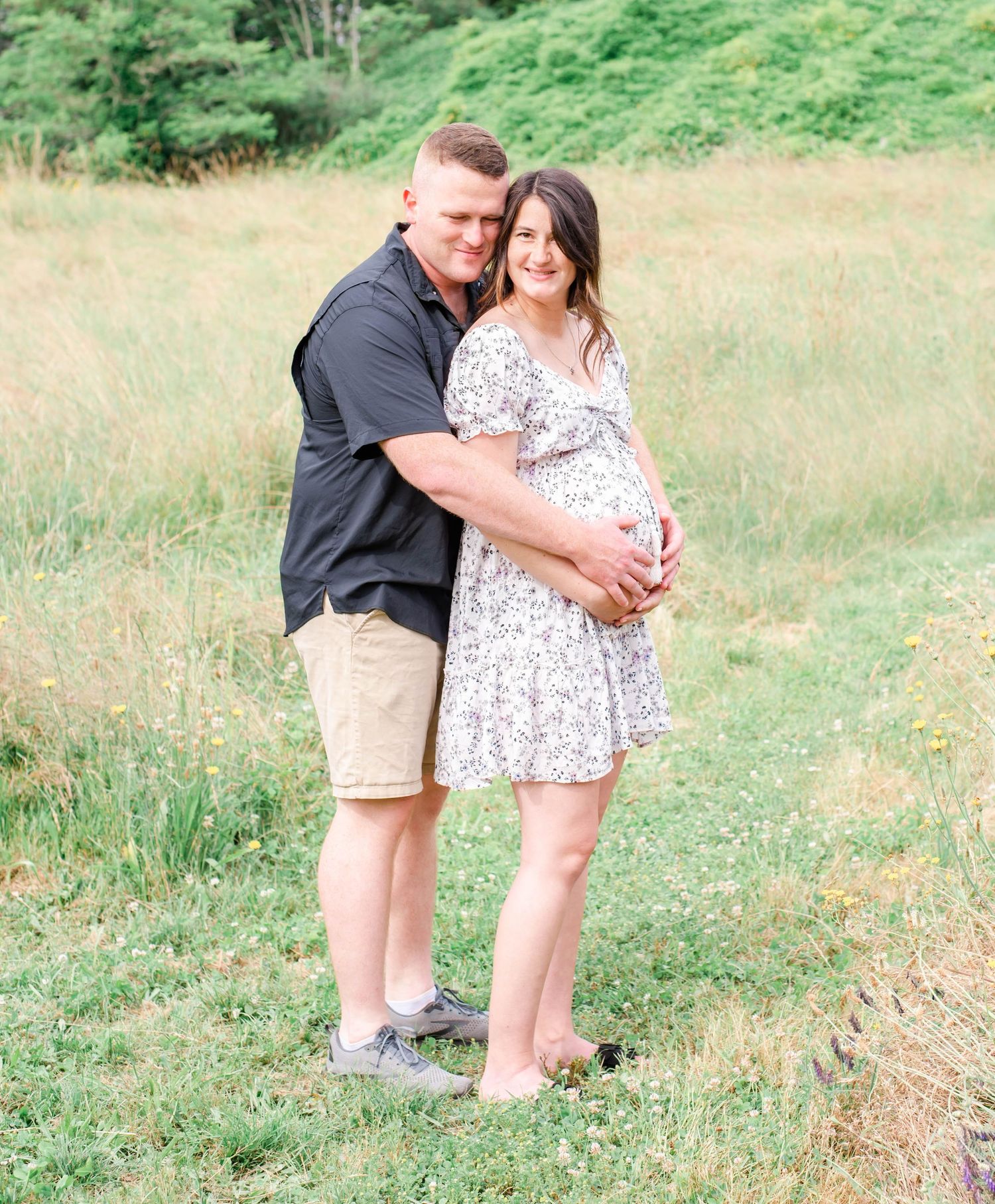 Loving couple's maternity photoshoot in a sunny meadow with natural scenery.
