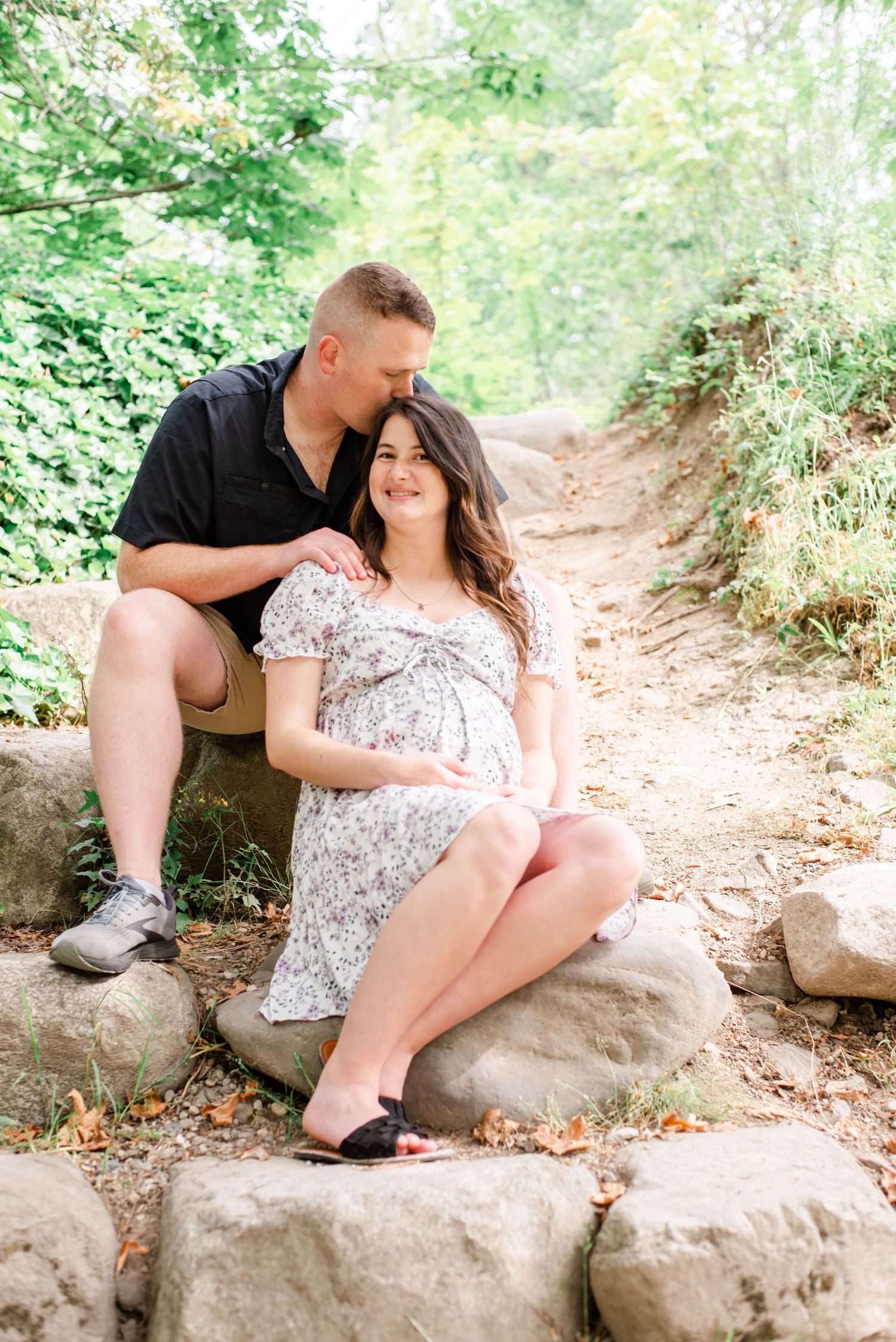Romantic couple sitting together on a rock trail surrounded by lush greenery.