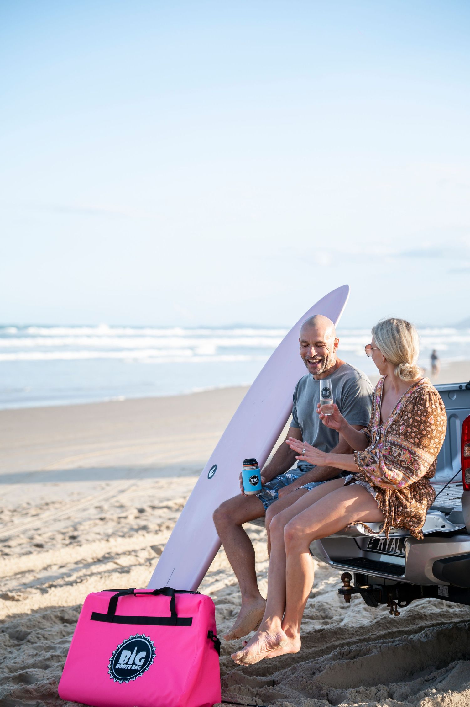 Beachside scene with surfboard and pink cooler bag on sandy shore.