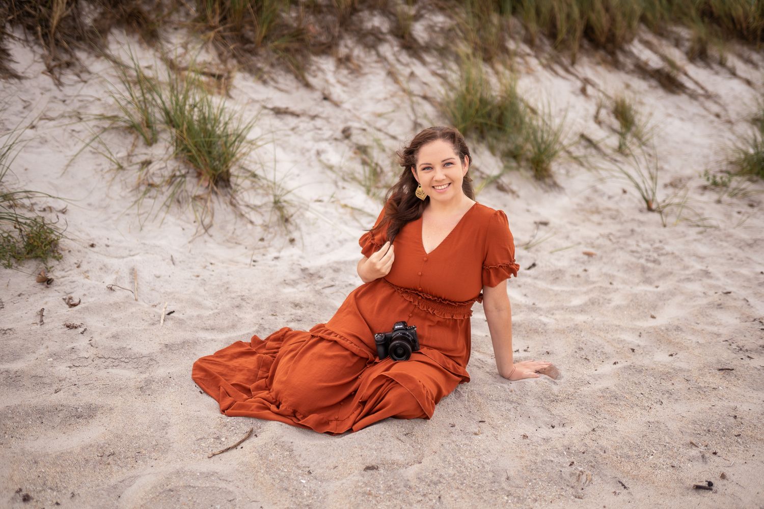 Photographer sitting on the beach in a orange dress with a camera in her lap Melbourne Cocoa Beach Vero Florida Branding Photoshoot