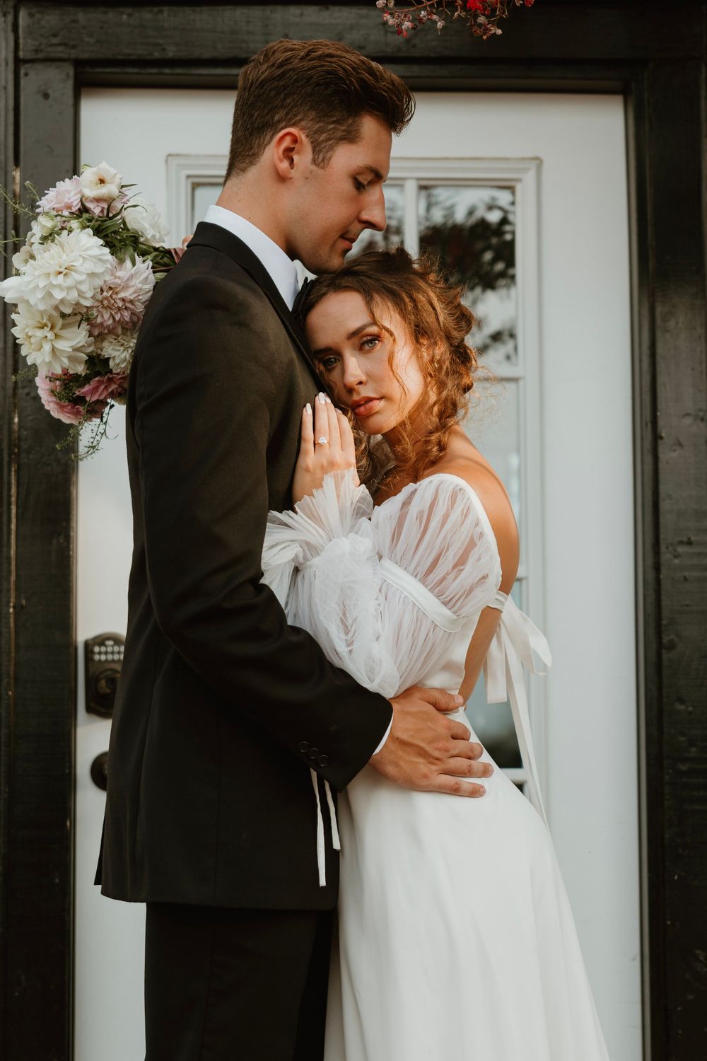 An intimate wedding portrait with a couple in formal attire against a white door.