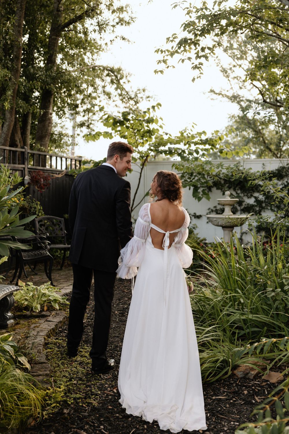 A bride and groom share a quiet moment on a garden path.